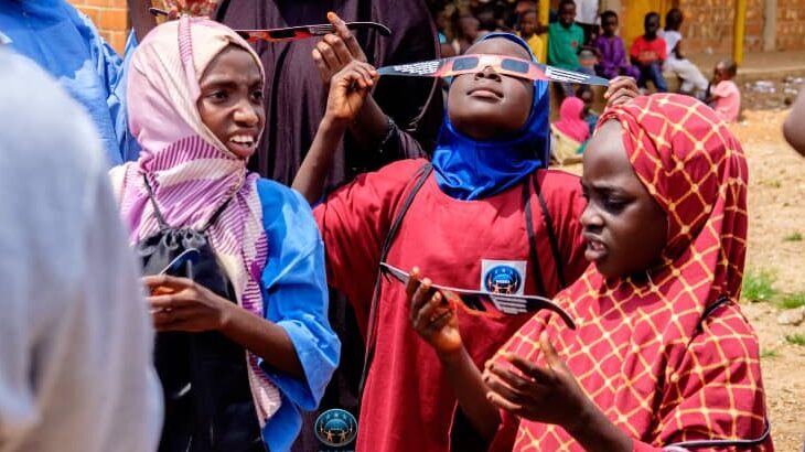 Three Nigeria girls view a solar eclipse through special glasses