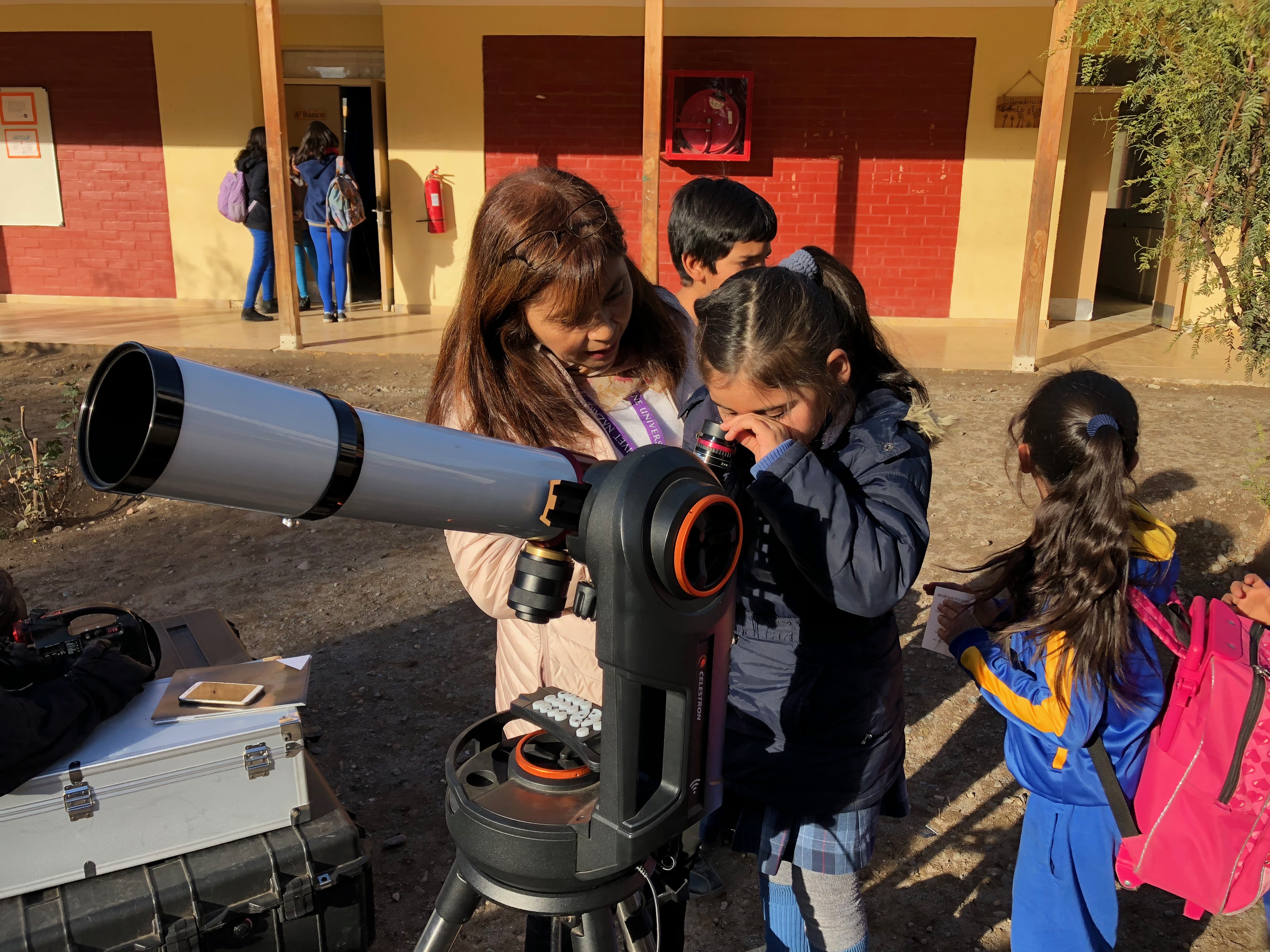An elementary-aged girl learns how to use telescope with guidance from an instructor.