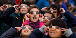 Group of children watch solar eclipse through special glasses.