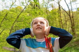 A young girl wearing over the ear headphones listens a to podcast outdoors