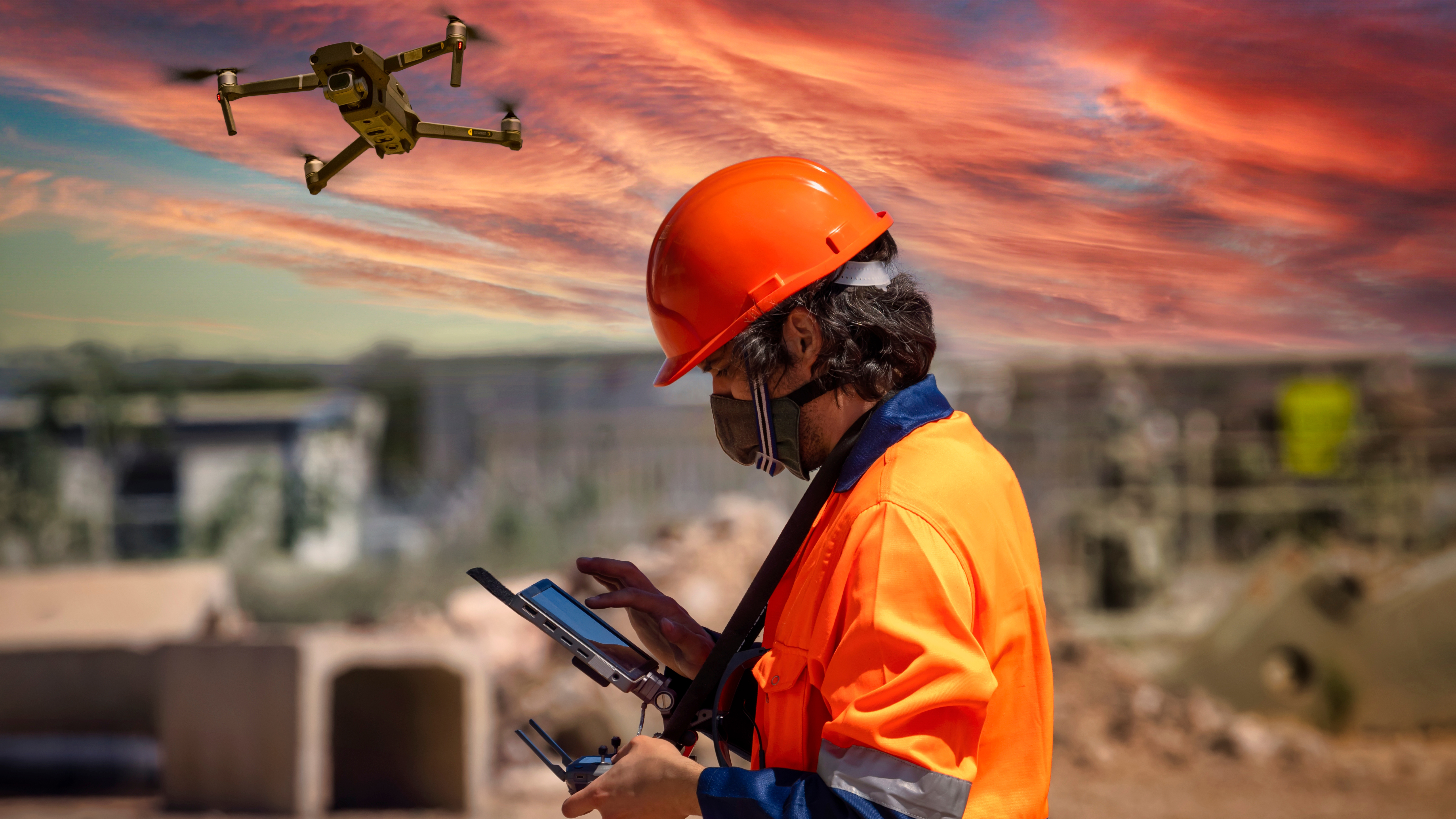 Man wearing a hard hat operates a drone at a mining facility.