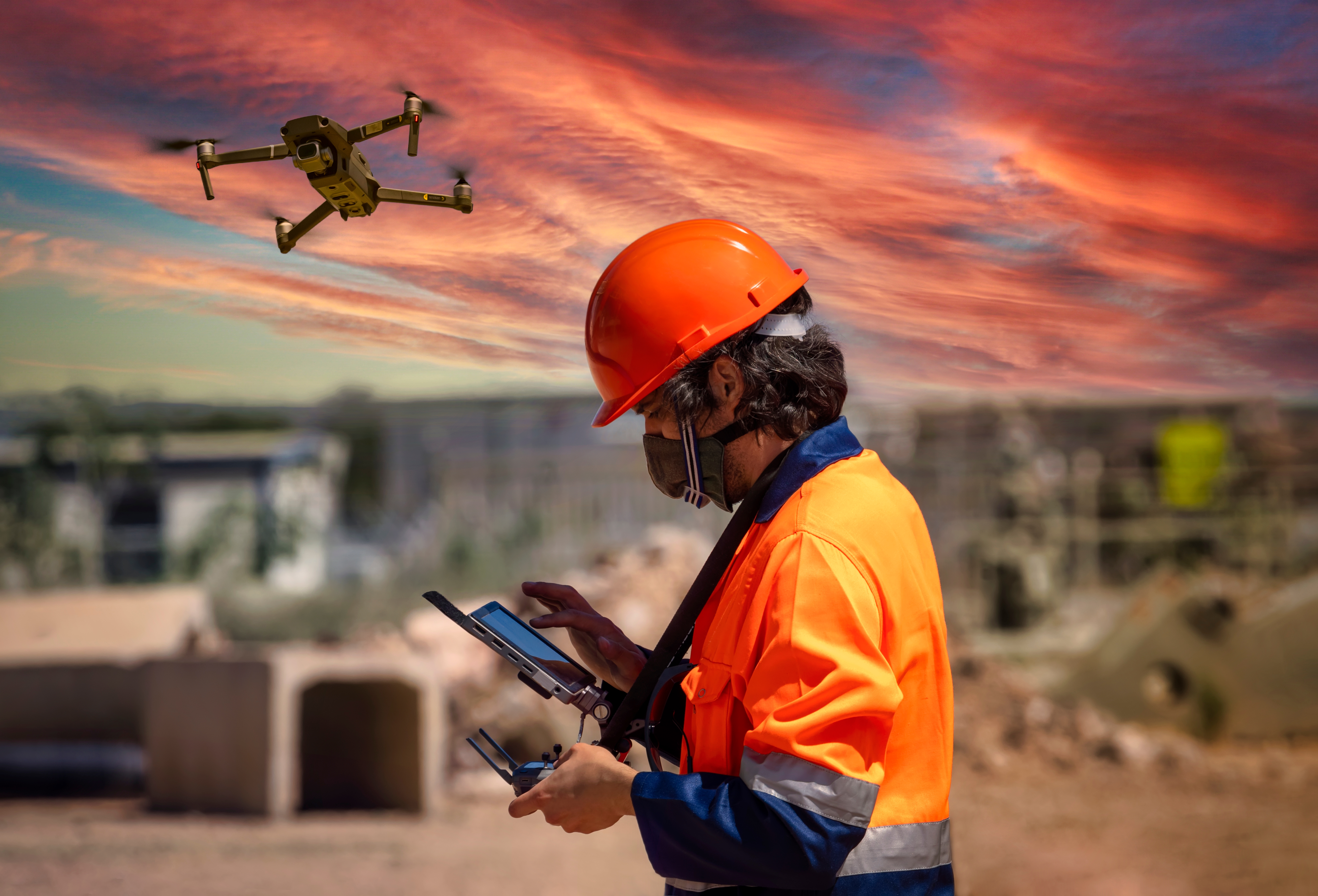 Man wearing a hard hat operates a drone at a mining facility.