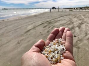 Hand stretched out with a pile full of nurdles. The coastline is in the background.