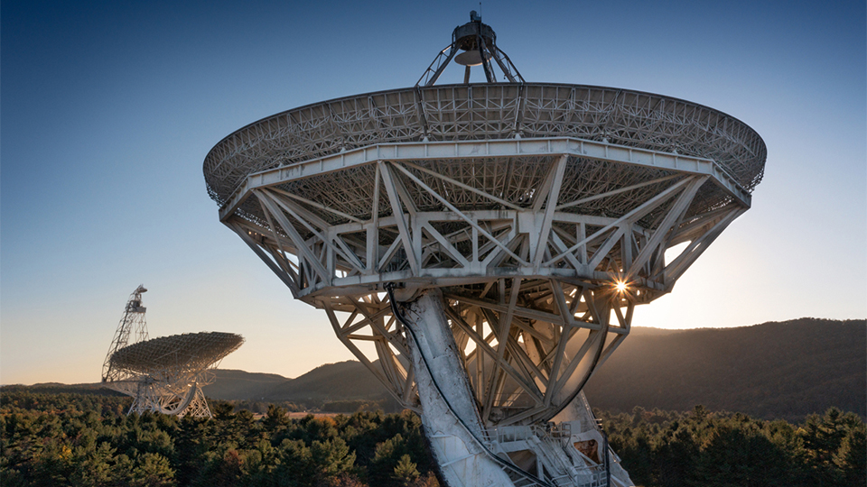 The sun sets behind two radio telescopes at the Green Bank Observatory.