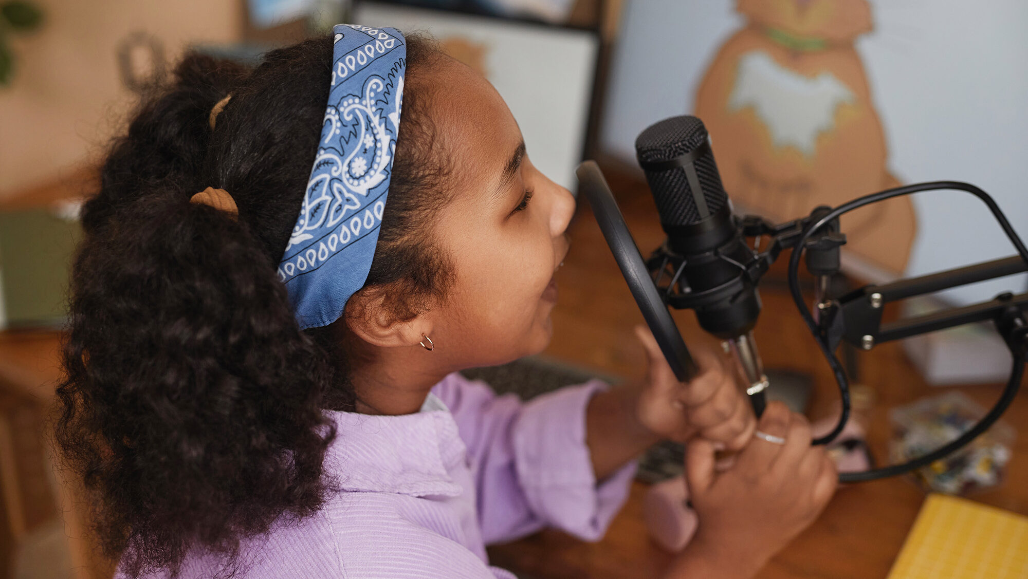 A young girls holds on to a studio mic and speaks into with a smile.
